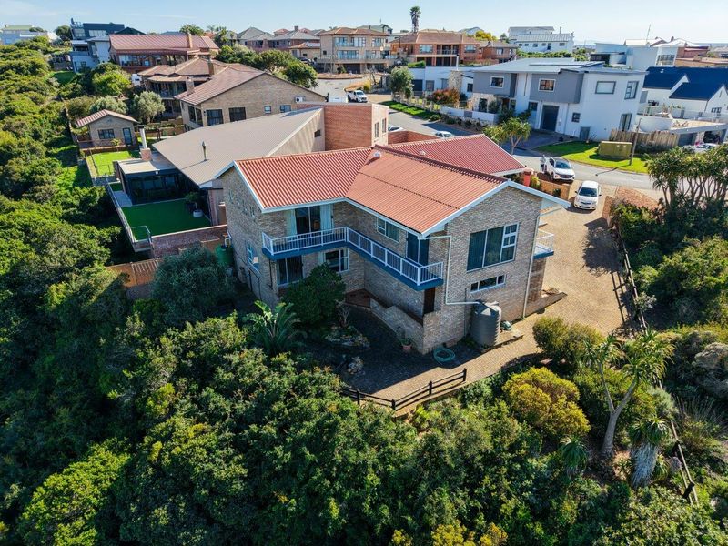 Aerial view of a multi-level brick house with a tiled roof, featuring a balcony and surrounding landscaped garden in a residential neighborhood.