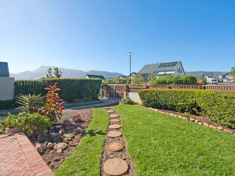 A well-maintained garden featuring a brick-paved area, a stone stepping path through the lawn, and established hedging with mountain views in the background.