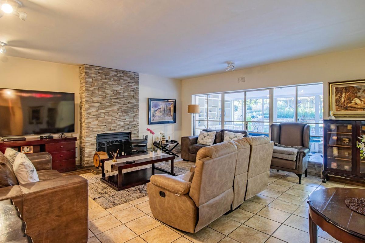 Spacious living room featuring a stone-clad fireplace, tiled flooring, and large windows providing natural light and access to the patio area.