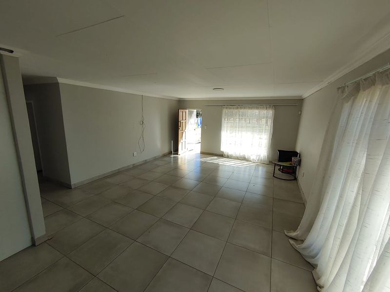 A spacious, empty living area featuring neutral tiled flooring and natural light, providing a blank canvas for interior design and personalization.