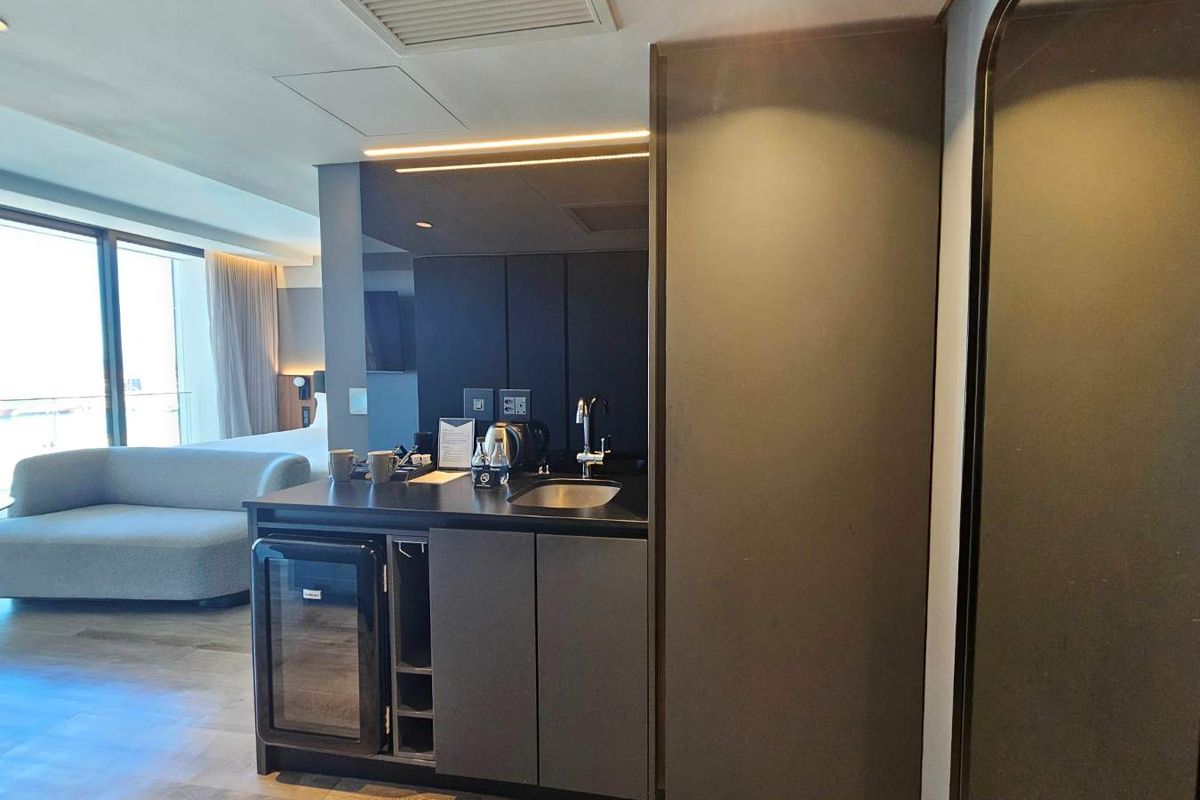 A modern, compact kitchenette featuring dark cabinetry, integrated under-counter refrigeration, a stainless steel sink, and sleek finishes, seamlessly integrated into an open-plan living space.