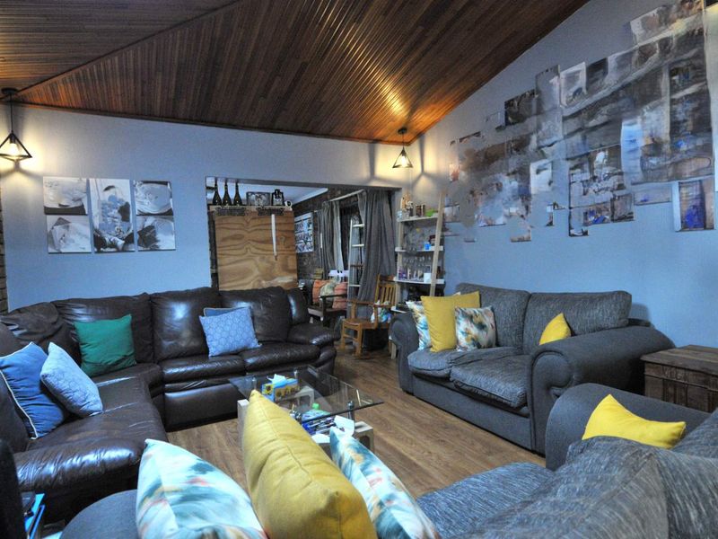 Spacious living room featuring a distinctive timber-clad vaulted ceiling, exposed brick accents, and warm laminate flooring, creating a cozy and inviting atmosphere.
