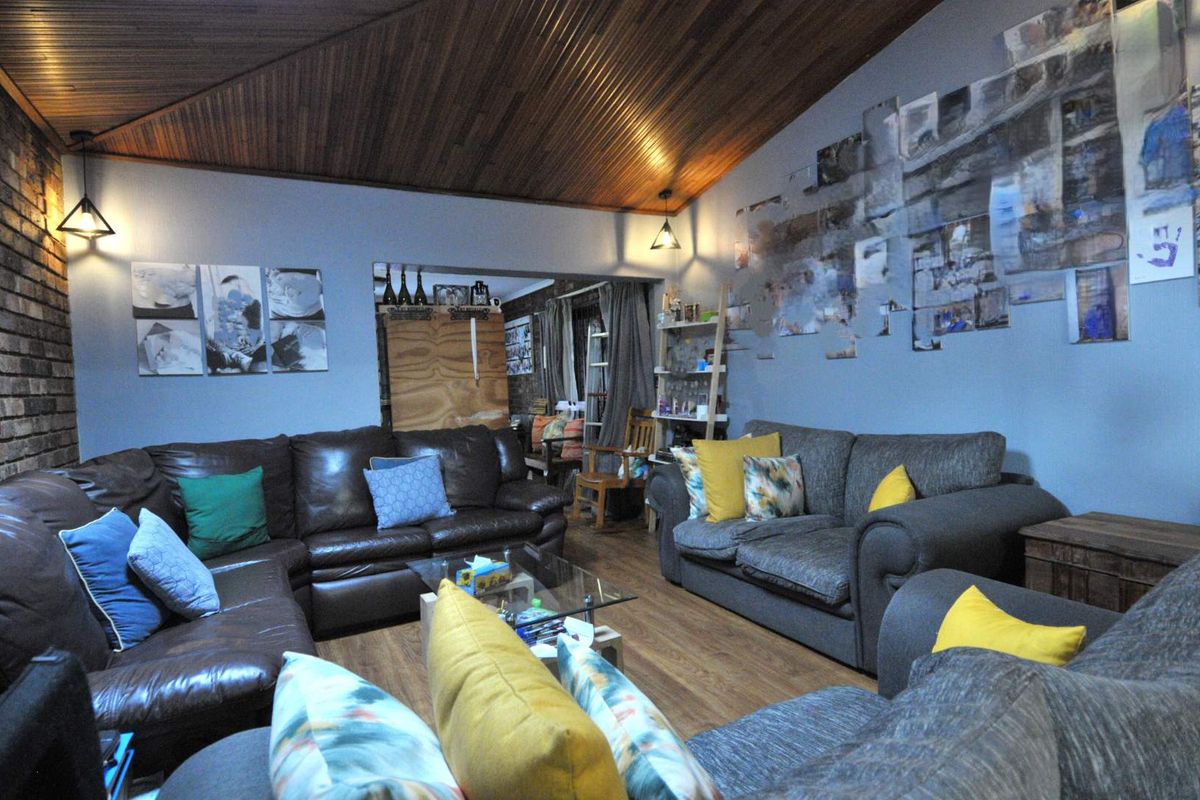 Spacious living room featuring a distinctive timber-clad vaulted ceiling, exposed brick accents, and warm laminate flooring, creating a cozy and inviting atmosphere.