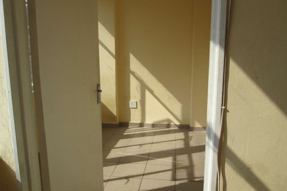 A view through a doorway into an empty, sunlit room featuring tiled flooring and plain yellow walls.
