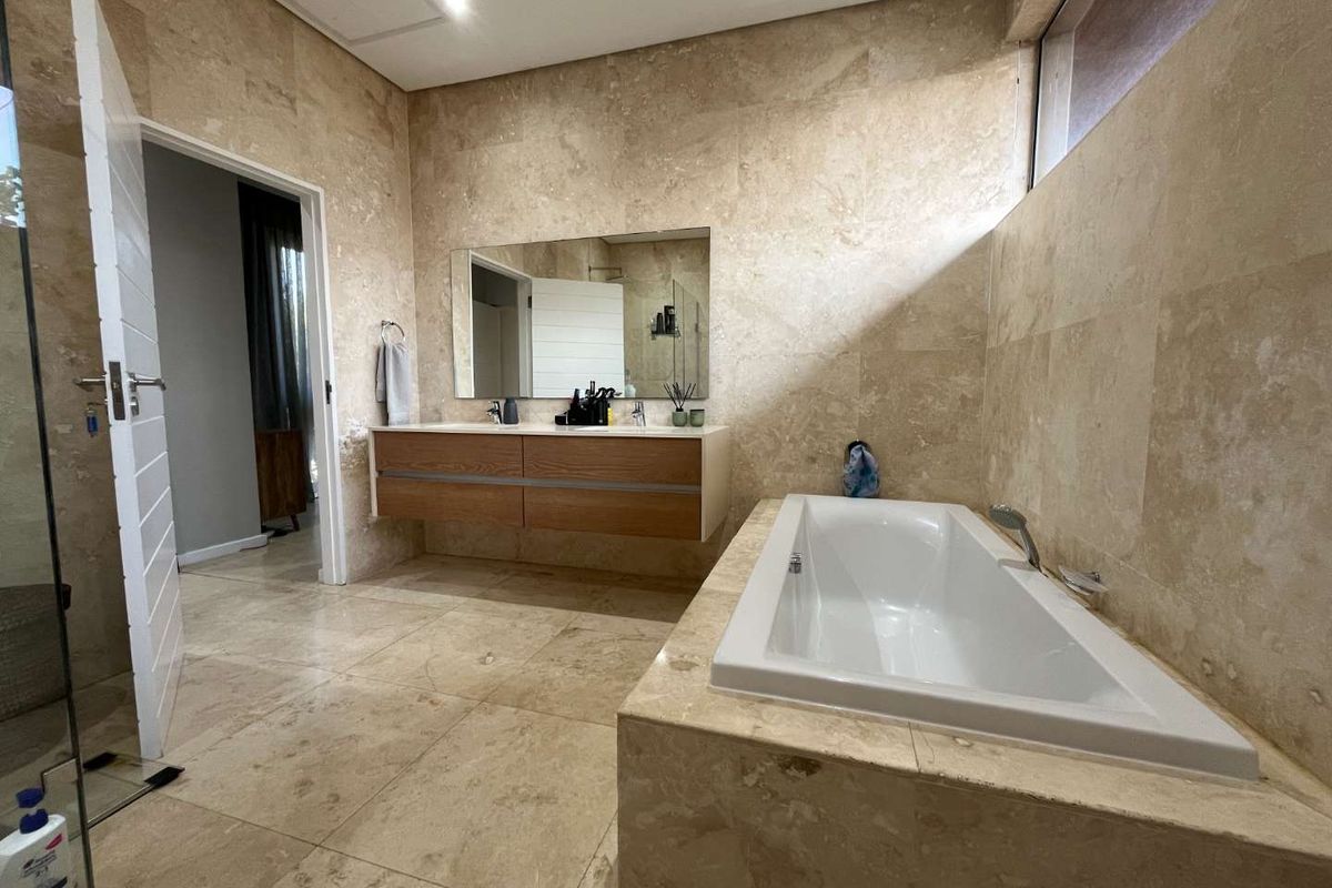 Modern bathroom featuring high-end travertine wall and floor tiling, a floating vanity, and a built-in bathtub with a glass shower enclosure.