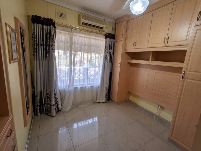 A bedroom featuring built-in wooden cupboards, tiled flooring, and an integrated air conditioning unit.