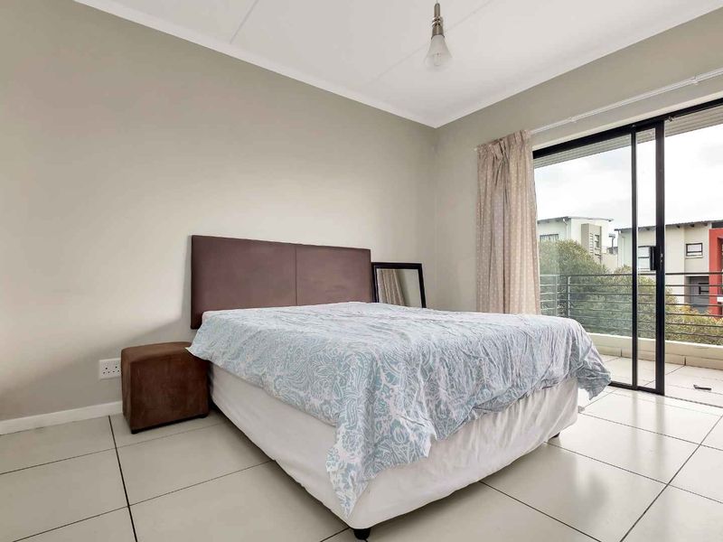A bright bedroom featuring neutral walls, tiled flooring, and a sliding glass door providing direct access to a private balcony.