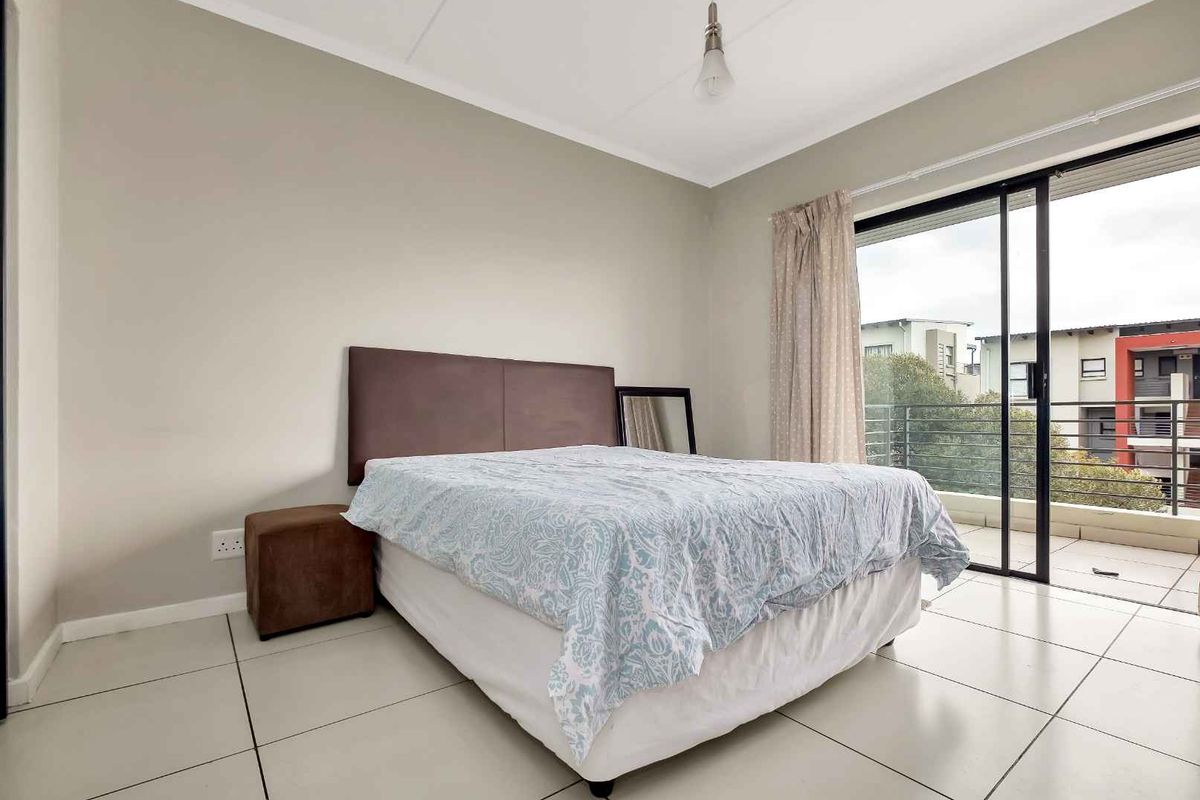 A bright bedroom featuring neutral walls, tiled flooring, and a sliding glass door providing direct access to a private balcony.