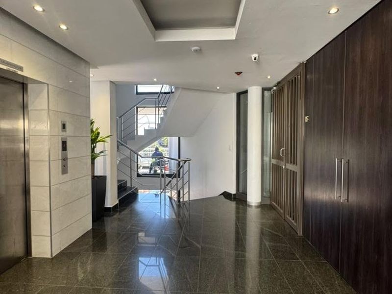 Modern office building entrance lobby featuring polished stone flooring, a sleek elevator, and a contemporary staircase with metal railings.