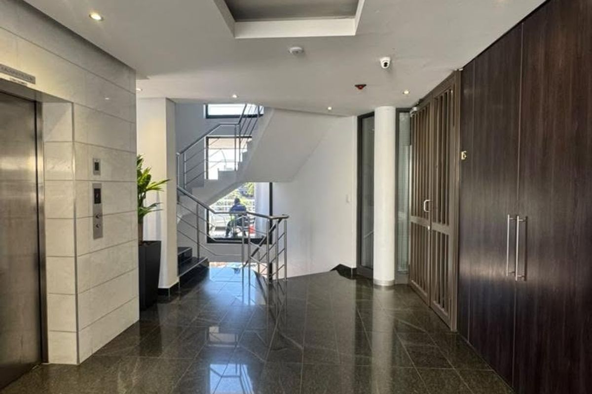 Modern office building entrance lobby featuring polished stone flooring, a sleek elevator, and a contemporary staircase with metal railings.