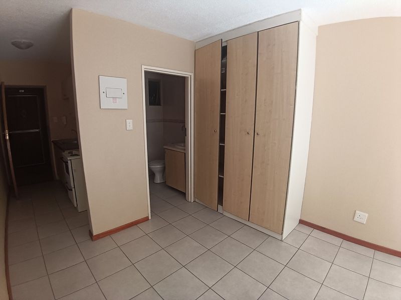 Open plan living area featuring tiled flooring and built-in cupboards, with direct access to an adjoining bathroom and kitchen area.