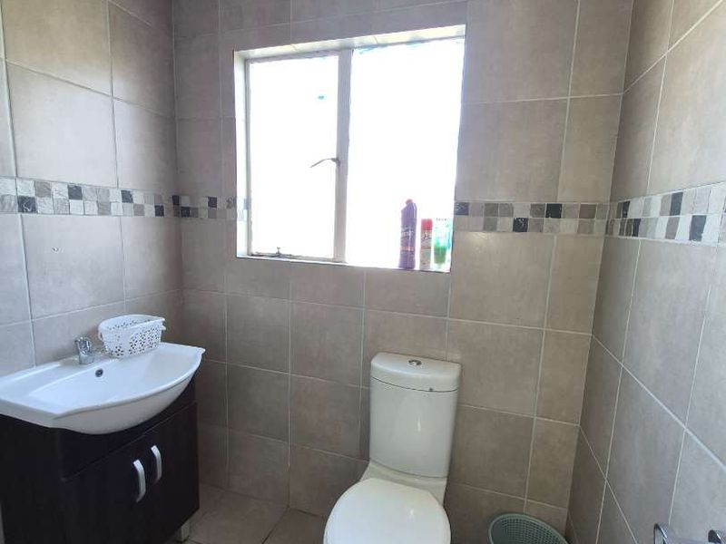 A functional bathroom featuring tiled walls and flooring, a vanity cabinet with a basin, and a standard toilet.