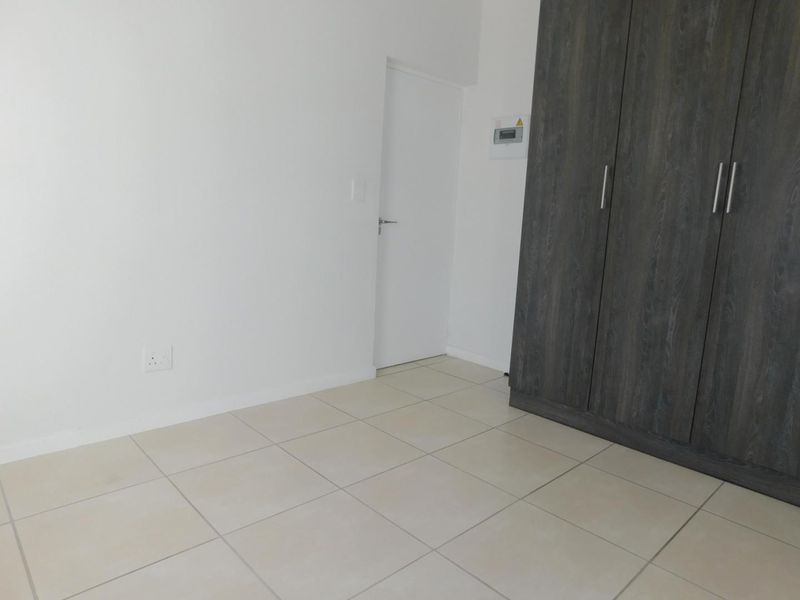 A clean, empty bedroom featuring neutral tiled flooring and modern dark wood built-in cupboards.