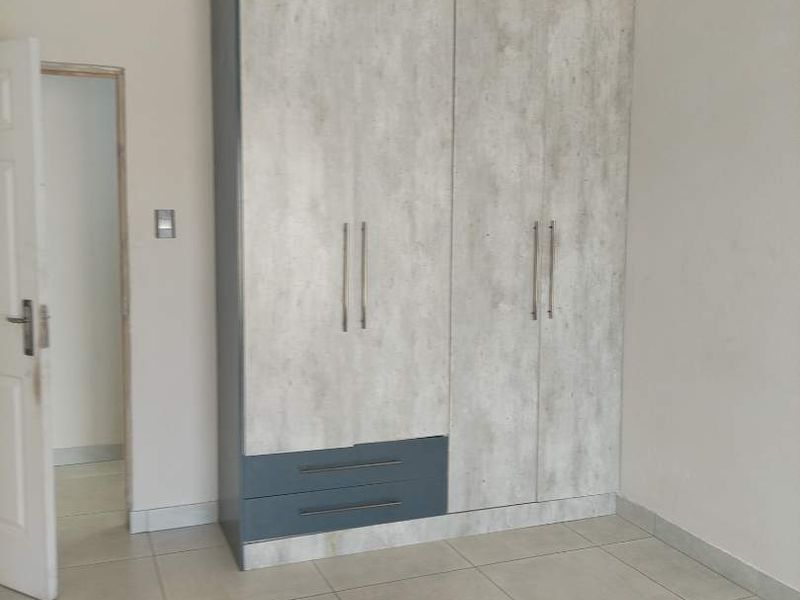 A clean, empty bedroom featuring modern built-in cupboards with a concrete-look finish and neutral floor tiles.