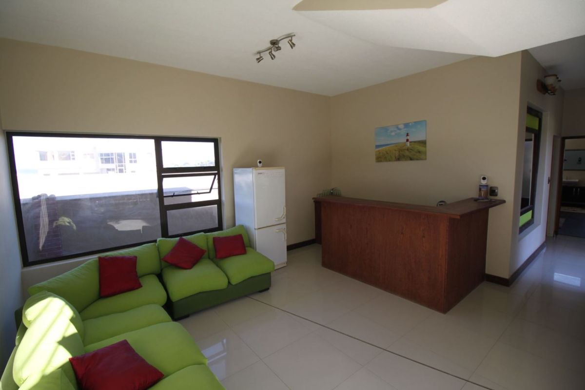 A living area featuring a built-in wooden bar counter, tiled flooring, and large windows providing natural light.