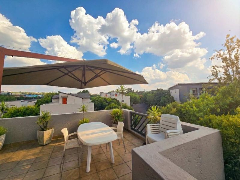 A spacious outdoor balcony featuring tiled flooring and a protective parapet wall, offering an open-air space for relaxation with neighborhood views.