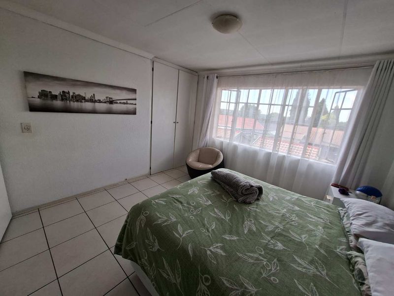 A functional bedroom featuring tiled flooring, built-in cupboards, and a large window providing natural light and neighborhood views.