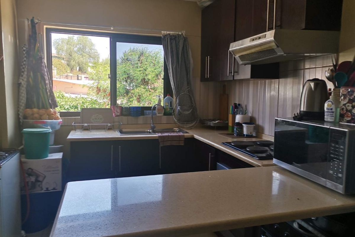 A functional kitchen featuring dark cabinetry, stone-look countertops, a built-in extractor fan, and a stainless steel sink with a window view.
