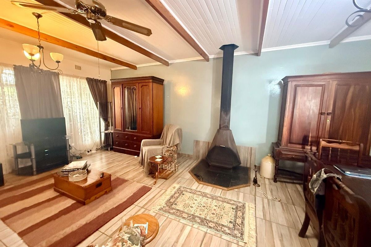 Spacious living room featuring exposed timber ceiling beams, a central freestanding fireplace, and tiled flooring throughout.