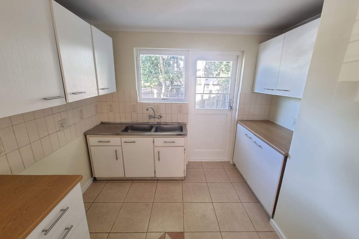 A functional kitchen featuring white cabinetry, laminate countertops, a double bowl sink, tiled splashbacks, and direct access to the exterior.