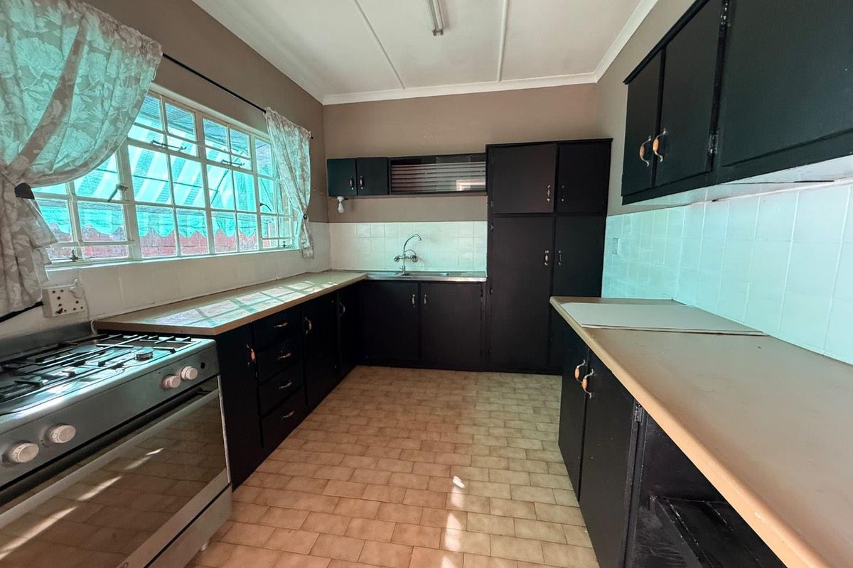 A functional kitchen featuring dark cabinetry, tiled countertops, a gas stove, and a stainless steel sink with a window view.
