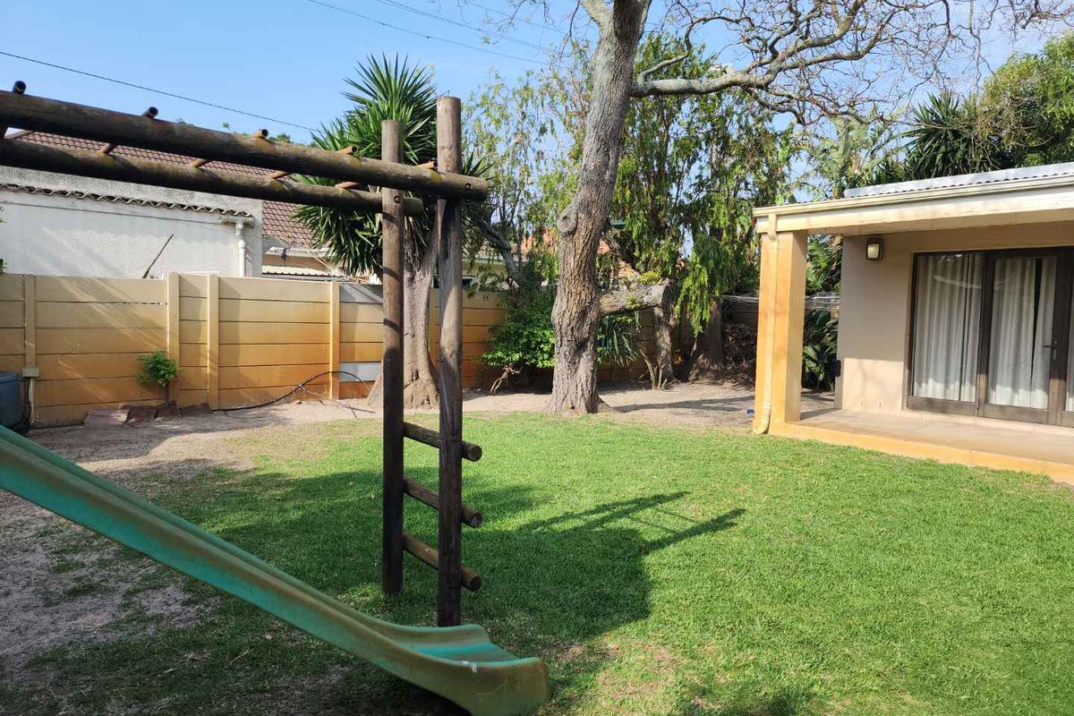 Rear garden featuring a lawn area, mature trees, and a covered patio with sliding glass doors, enclosed by a precast concrete boundary wall.