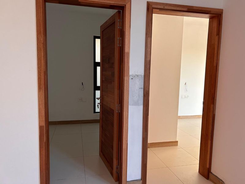 A hallway featuring tiled flooring and wooden door frames leading into two empty rooms with neutral walls and electrical fixtures.