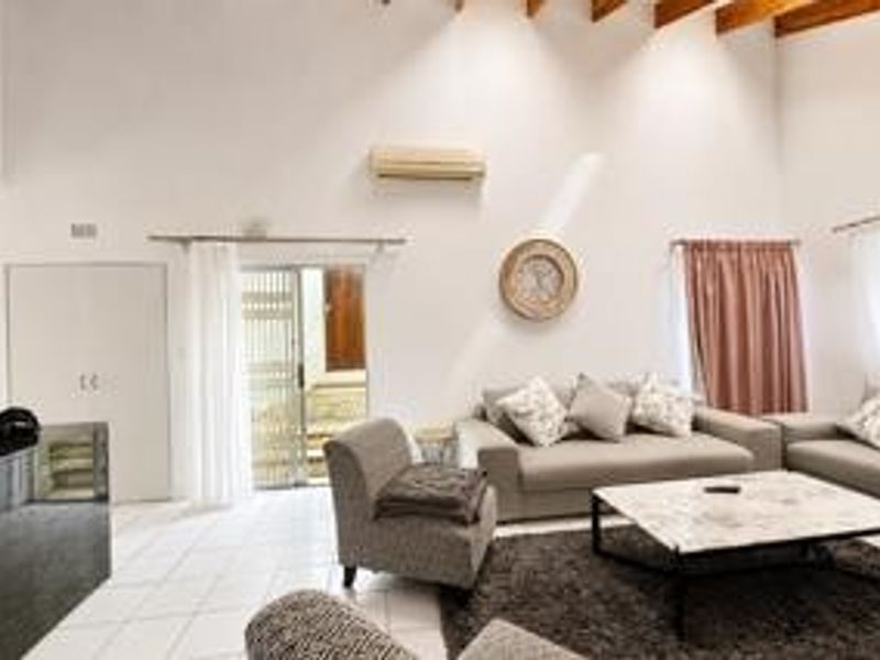 Spacious living room featuring high ceilings with exposed timber beams, tiled flooring, a split-system air conditioner, and direct access to an outdoor area.