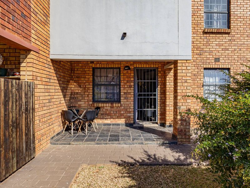 A rear exterior view of the apartment featuring a brick facade, a tiled patio area, and a secure entrance gate.