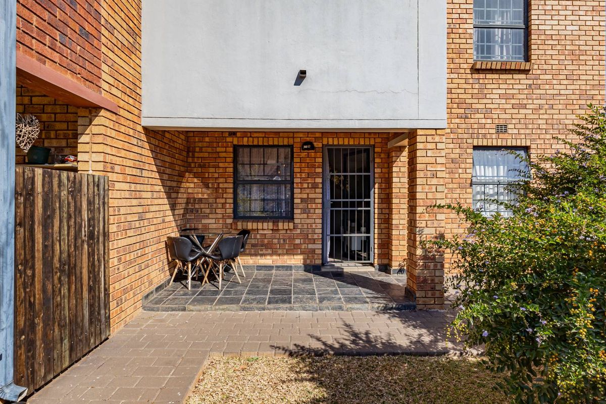 A rear exterior view of the apartment featuring a brick facade, a tiled patio area, and a secure entrance gate.