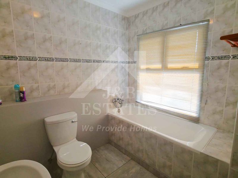 A functional bathroom featuring a built-in bathtub, ceramic wall and floor tiling, and a standard toilet suite.