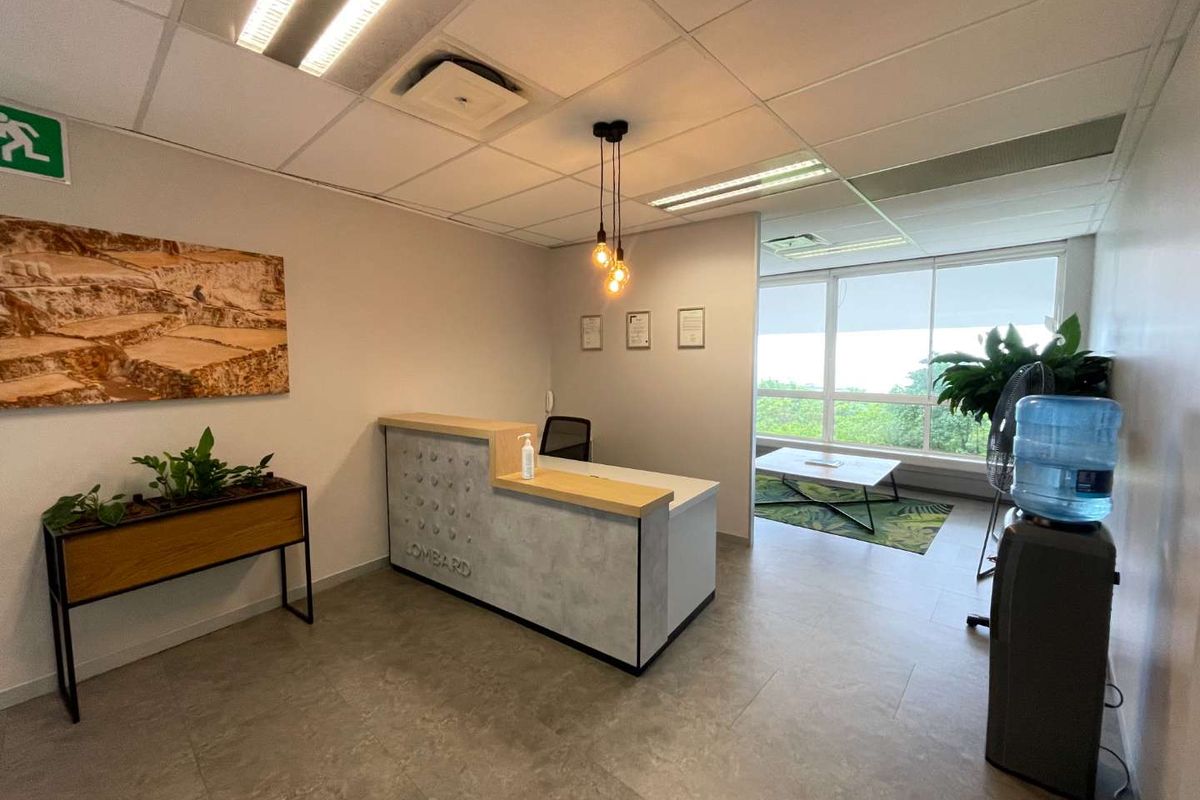 A professional office reception area featuring a modern built-in desk, tiled flooring, suspended ceiling, and large windows providing natural light.