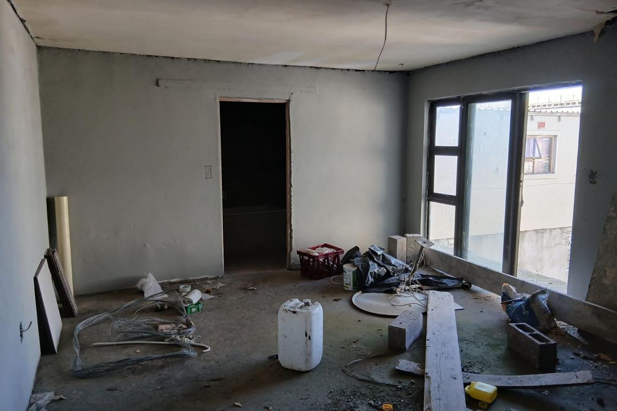 An unfinished interior room currently under renovation, featuring exposed concrete floors, raw plastered walls, and large windows awaiting final finishes.