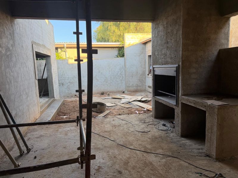 An unfinished outdoor patio area under construction, featuring a built-in braai and raw concrete masonry, awaiting final finishes and landscaping.