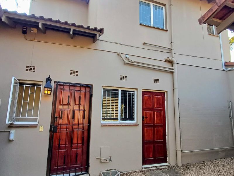 Rear exterior view of the townhouse featuring timber doors with security gates, security bars on windows, and exposed external plumbing.