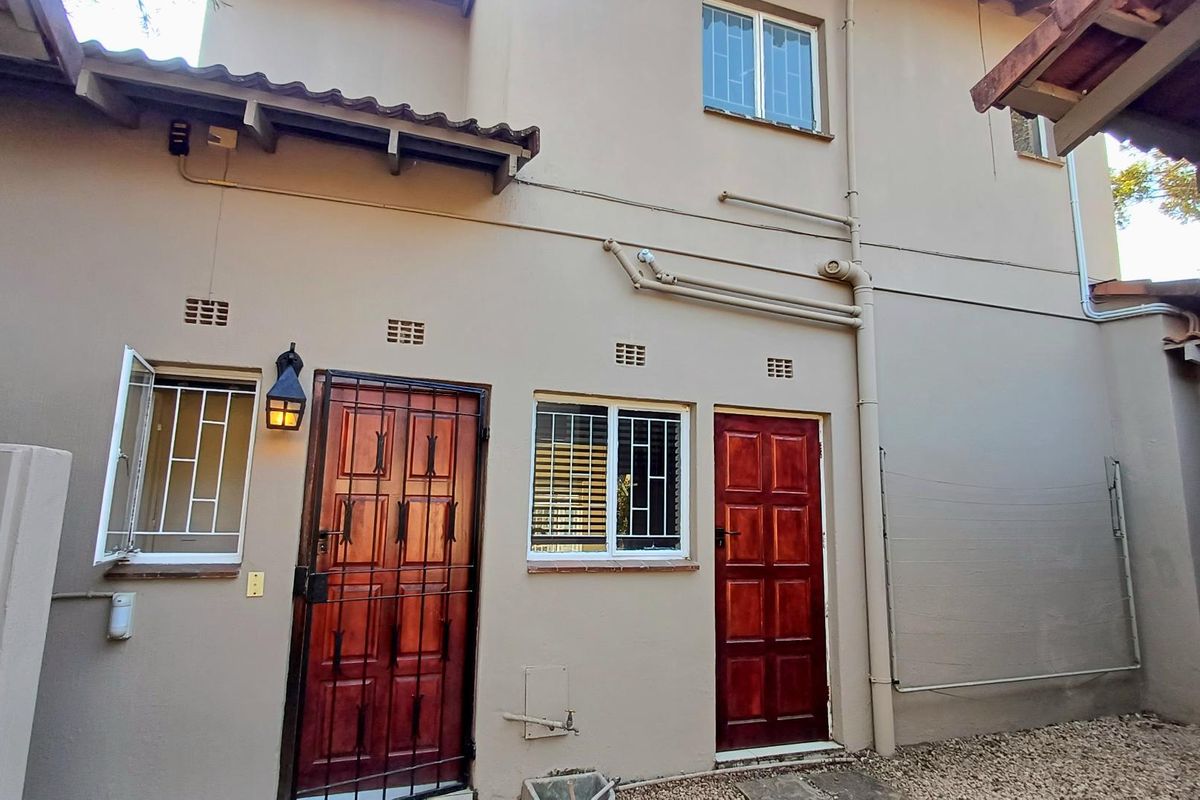 Rear exterior view of the townhouse featuring timber doors with security gates, security bars on windows, and exposed external plumbing.