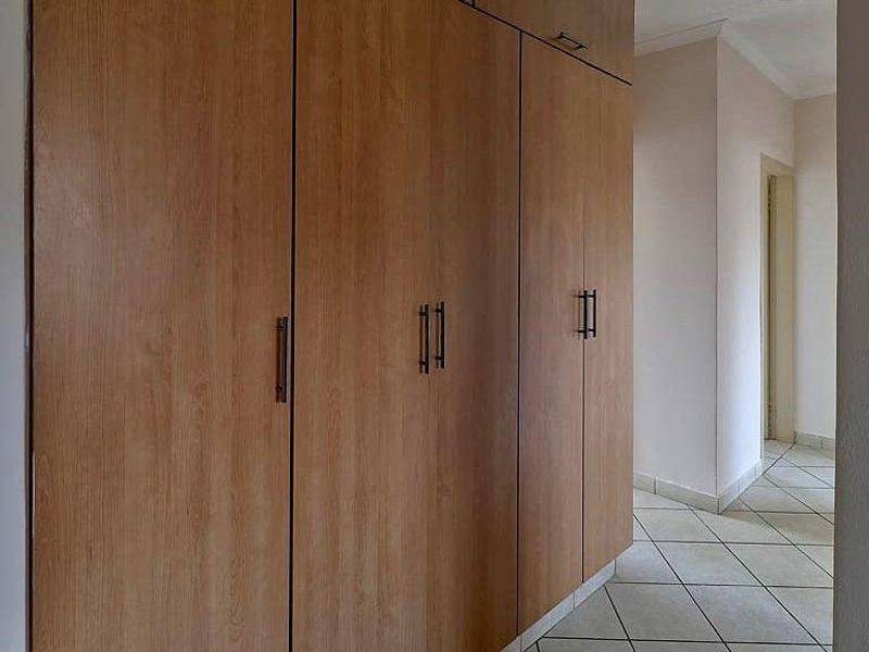 A functional hallway featuring extensive built-in wooden cabinetry and neutral tiled flooring, providing ample storage space within the apartment.