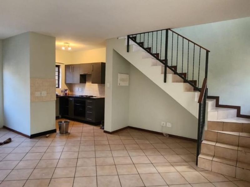 Open-plan living area featuring tiled flooring, a staircase with metal balustrade, and a functional kitchen with built-in cabinetry and appliances.