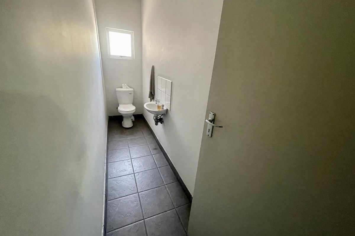 A functional, compact industrial-style restroom featuring a toilet, wall-mounted basin with tiled splashback, and durable tiled flooring.