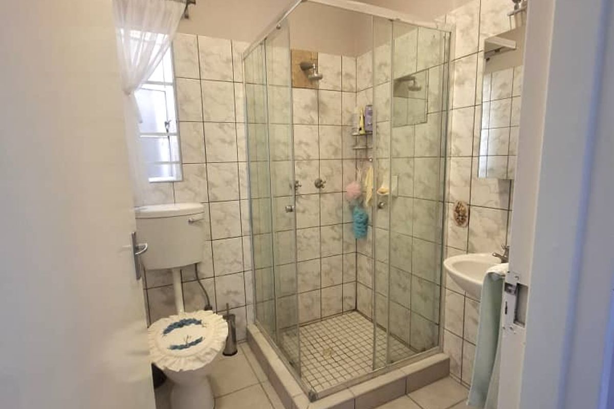 A functional bathroom featuring a corner glass shower enclosure, a standard toilet, and a wall-mounted basin with tiled flooring and wall finishes.