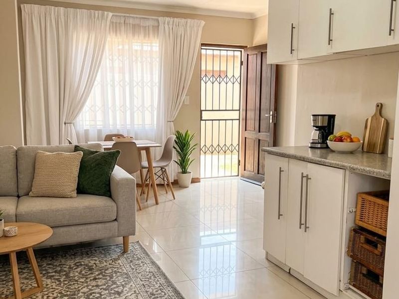 Bright open-plan living and kitchen area featuring modern white cabinetry, tiled flooring, and direct access to the exterior through a secure entrance door.