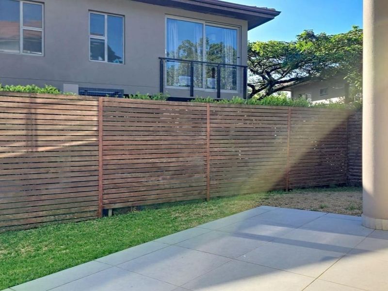A private rear garden area featuring a tiled patio, timber slat fencing, and a view of the townhouse exterior with sliding door access.