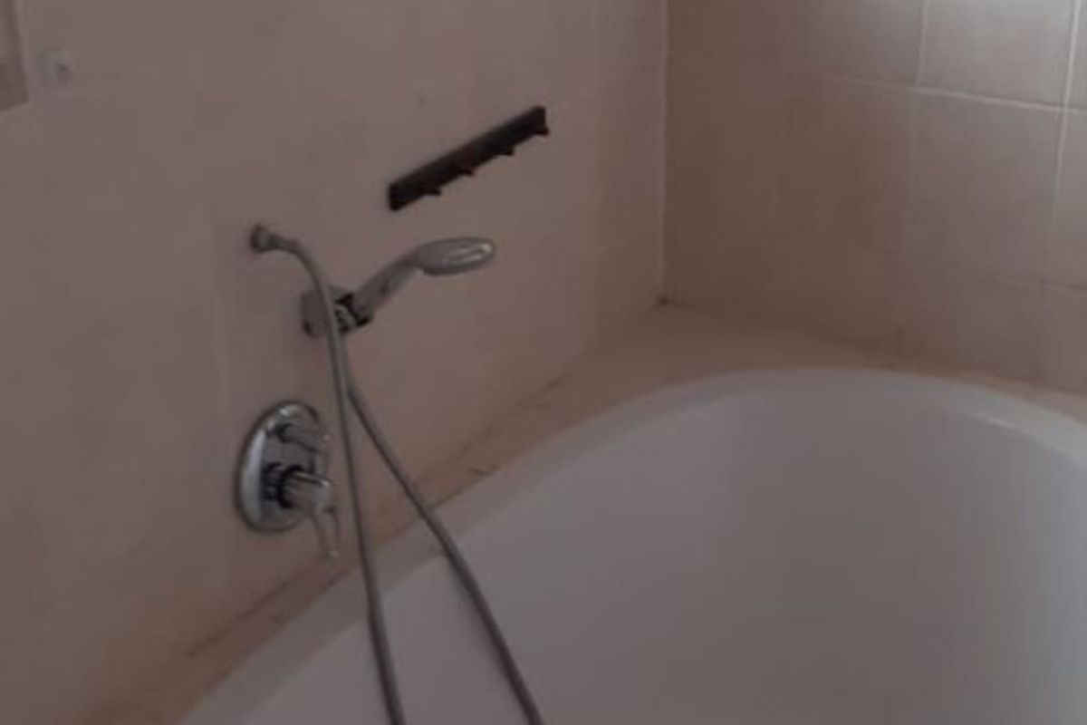 A functional bathroom featuring a built-in oval bathtub with a handheld shower mixer, tiled walls, and a window with security bars.