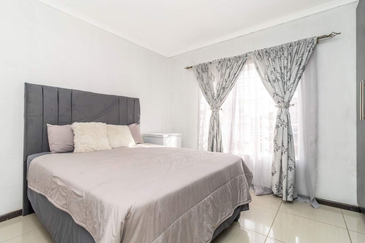 A bright bedroom featuring neutral tiled flooring, white walls, and a window fitted with curtain rods.