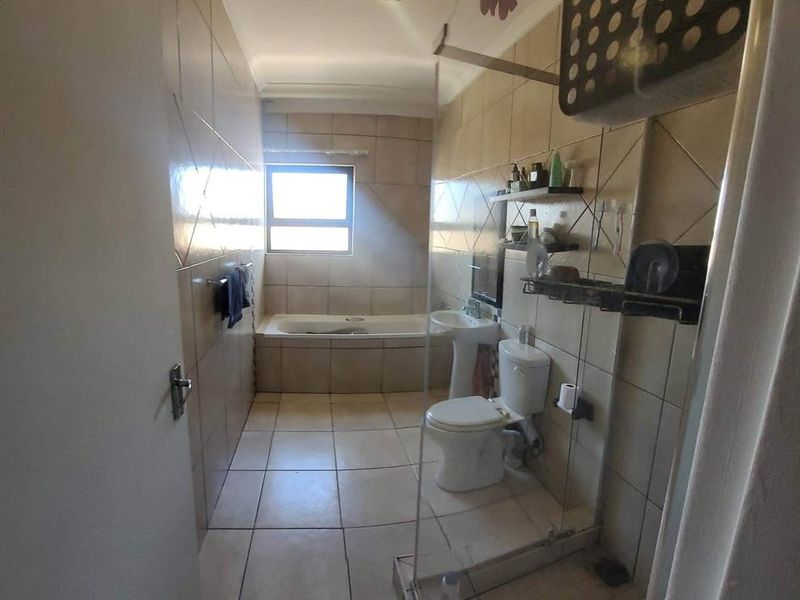 A functional bathroom featuring a bathtub, pedestal sink, toilet, and a glass-enclosed shower with neutral wall and floor tiling.