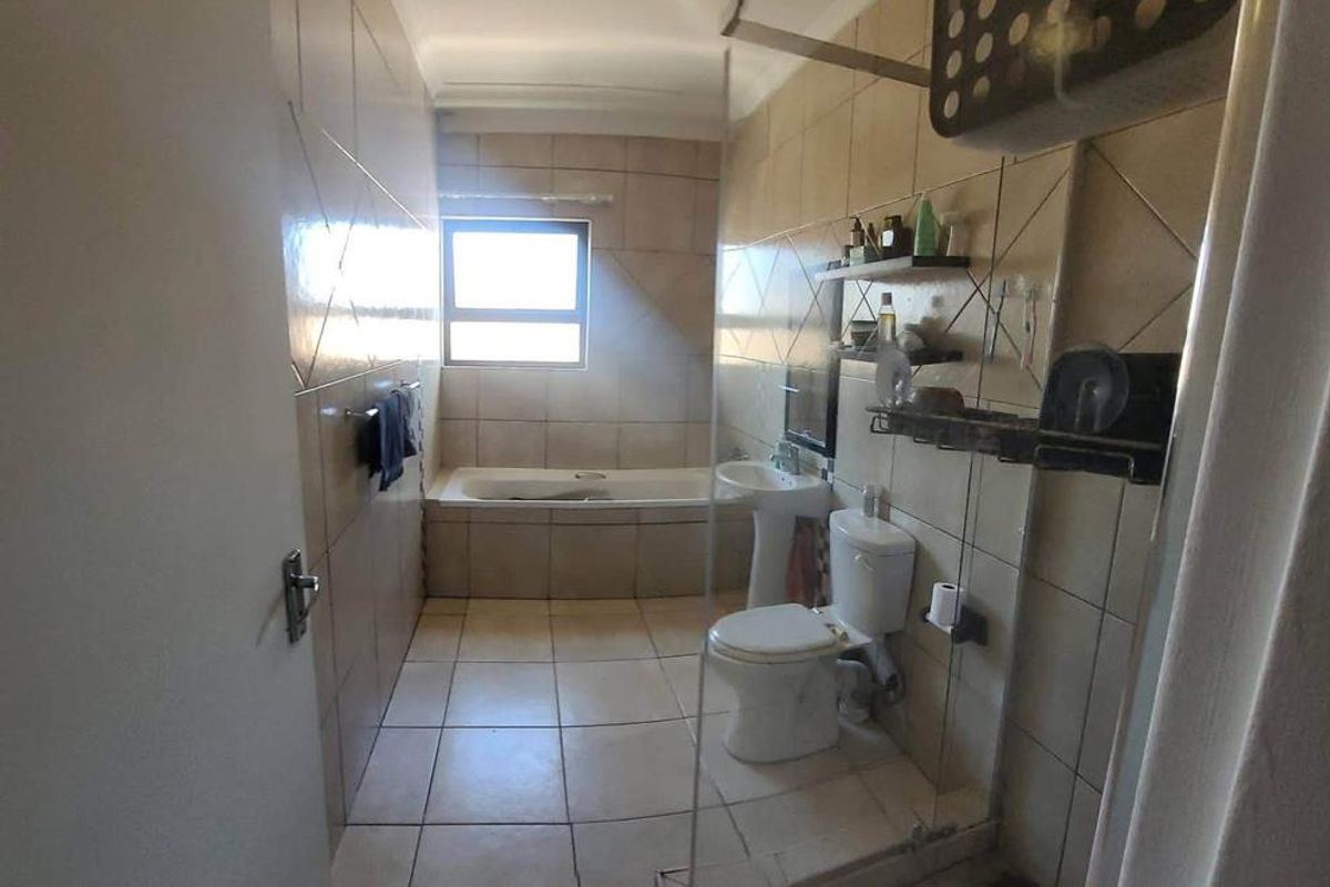 A functional bathroom featuring a bathtub, pedestal sink, toilet, and a glass-enclosed shower with neutral wall and floor tiling.