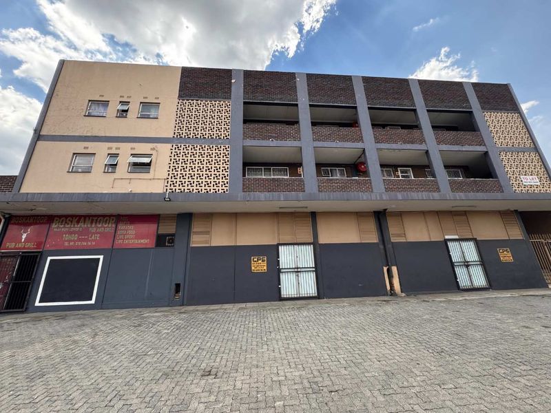 Front elevation of a multi-story mixed-use building featuring a paved driveway, ground-level commercial frontage, and upper-level residential balconies with decorative brickwork.