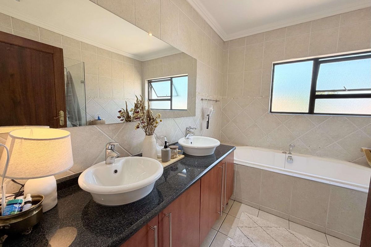 A well-maintained bathroom featuring a double vanity with granite countertops, vessel sinks, a built-in bathtub, and neutral wall tiling.