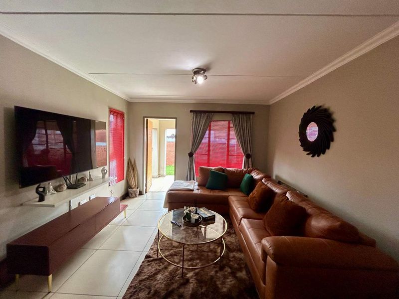 A well-maintained living room featuring tiled flooring, neutral wall tones, and natural light through windows fitted with venetian blinds and curtain tracks.