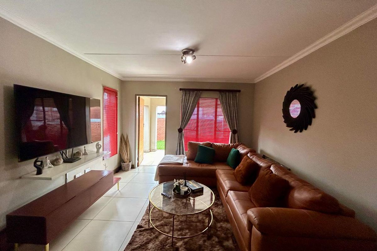 A well-maintained living room featuring tiled flooring, neutral wall tones, and natural light through windows fitted with venetian blinds and curtain tracks.